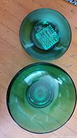 Two green glass bowls, one larger salad bowl with pressed starburst pattern and one smaller smooth-edged bowl, both translucent green glass