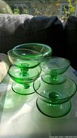 Four green glass dessert dishes stacked, showing their round bowls and pedestal bases in translucent green glass.