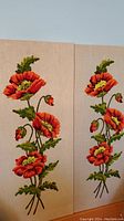 Two hand stitched wall hangings showing red-orange floral design with green leaves on beige canvas.