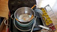 Photo showing assorted kitchen pans, bowls, and tools including a metal roasting pan, mixing bowls, and strainer