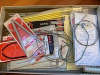 Top-down photo of knitting needles lot showing mix of packaged and loose needles including yellow plastic and metal circular needles