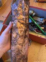 Rolled copper sheeting held in hand, showing dents and staining consistent with aged metal sheet.