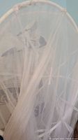 Photo showing the white mosquito net with circular frame, displaying mesh fabric and frame details.