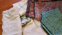 Overview of assorted tablecloths and placemats overlapping showing variety in fabric and crocheted textures