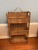 Front view of small three-tier wicker shelf showing construction and broken top left corner