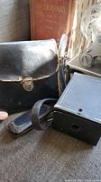 Vintage binoculars with leather carrying case and Kodak Brownie camera beside vintage book.