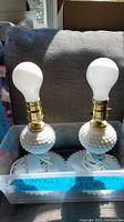Pair of vintage white glass hobnail textured lamps with brass bulbs in a box, no shades included.