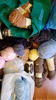 Various yarns in a green bag and spread on floor including pink, yellow, tan, gray, brown and multicolor yarns.