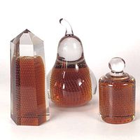Photo of trio of Bohemian crystal paperweights, pear, obelisk, and bell, showcasing amber color and bubbles