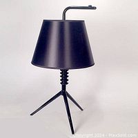 Front view of gloss black metal table lamp showing conical shade, turned spool‐like base on tripod legs.
