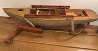 Side view of a wooden primitive boat model showing seat details and hanging straps.