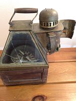 Front left perspective showing wooden base, brass top, folding handle and front glass panel with interior compass.