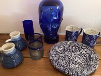 Full lot including blue glass head sculpture, three blue glasses, two floral patterned ceramic mugs, two measuring cups with floral design, and two matching floral plates.