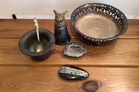 Overview of all items on wooden table showing bowl with spoon, decorative silver plate bowl, brass wolf head sculpture, two fossil rocks, and small silver plated bowl.