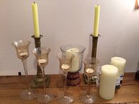 Full set showing two solid brass taper candle holders, four glass long stemmed votive holders, one large glass pillar candle holder with wicker base, and three pillar candles.