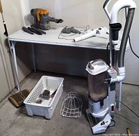 Full view of Shark upright vacuum with hose and brush, Dyson handheld vacuum, plastic basket with parts, ball cap holder, and broom and dustpan set.