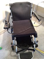 Front view of electric wheelchair with cushioned black seat, joystick controller on right side and footrest visible