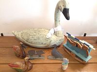 Full view of large wooden swan, two smaller painted wooden ducks, tin farm animal figures (pig and bird), and vintage blue wooden toy rocking boat with two rowers and two oars, plus small painted flower on cork base.