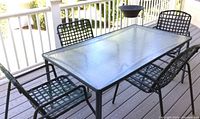 View showing the rectangular glass patio table with four dark green vinyl woven chairs around it on a wooden deck.