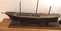 Side view of the wooden boat model showing the full hull, deck details including three masts and the wooden base.