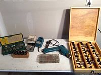 Overview of lot showing wooden case with router bits, Ace taps and dies set in green box, power drill, and small drill bits.