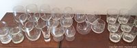 Wide view of all 22 glasses including snifters, stemmed glasses and highball glasses arranged on table