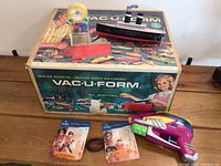 Photo showing the Vac-u-Form box with the plastic molding machine, a black and red Titanic model, and two Pixar Incredibles figures in packaging.