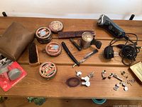 Full lot overview on wooden table showing the straight razor with strap, various tins of Kiwi shoe polish, shoe brushes, metal applicator tool, electric Norelco shaver, and sets of cuff links and tie clips.