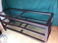 Full view of rectangular wood and glass display table showing dark wood frame, glass top, lower shelf, and leg structure.