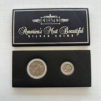 Top view showing the black case with the cover titled '1934 America's Most Beautiful Silver Coins'. Inside the case, two coins visible in plastic holders: a large Walking Liberty half dollar and a smaller Mercury dime.