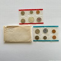 Two sets of sealed 1970 US proof coins in plastic strips laid out with original envelope included, showing worn condition of envelope and mint marks on tokens.