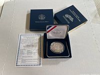 Photo showing the silver coin in its open blue United States Mint presentation box, the outer box, and the certificate of authenticity.
