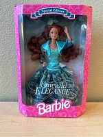 Front view of Special Edition Emerald Elegance Barbie doll in original pink box with clear plastic window. Doll is wearing turquoise and teal gown with floral metallic accents and matching jacket.
