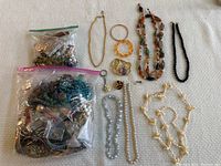 Photo shows the entire lot of assorted jewelry including necklaces, bracelets, rings, earrings and two bags packed with more mixed jewelry pieces.