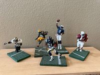 Five McFarlane NFL player models on green bases showing team colors and details.