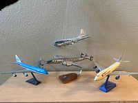 Four airplane models displayed on wooden surface. KLM on black stand, United suspended by wires, Pan American on wooden block stand, Eastern on blue stand.