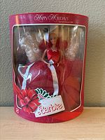 Front view of 1988 Happy Holidays Special Edition Barbie doll in original red packaging, doll visible inside wearing red glittery dress with white ribbon, festive graphics on box.
