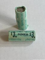 Two rolls of dimes wrapped in blue paper with printed Harrah's logos and $3 denomination, laid on white surface.