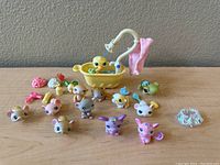 Collection of 16 Littlest Pet Shop small animal figures with various colors, a yellow bathtub accessory with duck and showerhead, pink towel, and a clear plastic circular piece accessory arranged on a flat surface.