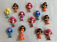 Photo of thirteen plastic Strawberry Shortcake character figurines in assorted poses and colors on fabric surface.