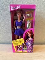 Front view of vintage Teresa Barbie doll in original pink box, doll dressed in purple with silver belt, accessories visible.