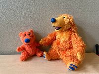 One photo showing the two orange cartoon bear plush toys, larger bear with curly fur and smaller with short fur.