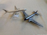 Two small airplane models side by side on a textured surface, showing Abercrombie & Kent model jet and United Airlines propeller plane