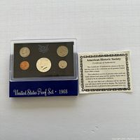 Photo showing complete United States Proof Set from 1968 in black and blue protective case with six proof coins visible, accompanied by certificate of authenticity from American Historic Society.