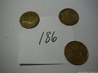 Three Canadian Loonie coins on white background near paper with lot number 186, showing both sides and overall condition.