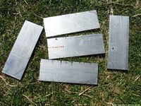 Five rectangular 6061 aircraft-grade aluminum plates laid on grass, clearly showing their flat, smooth metallic surfaces and size.