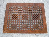 Single old cast iron grate showing a symmetrical geometric lattice pattern and rusted surface