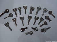 Photo showing 19 assorted antique metal keys with various shapes and rusted surfaces, arranged on a white background.