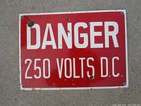 Red enamel metal sign with bold white text: 'DANGER 250 VOLTS D.C.' showing paint chips and rust spots.