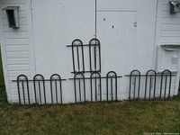 Four black aluminum garden fencing panels arranged against a white shed wall, showing size variation.